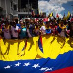 Uno scatto in cui i manifestanti si riuniscono intorno a una grande bandiera del Venezuela Uno scatto in cui i manifestanti si riuniscono intorno a una grande bandiera del Venezuela