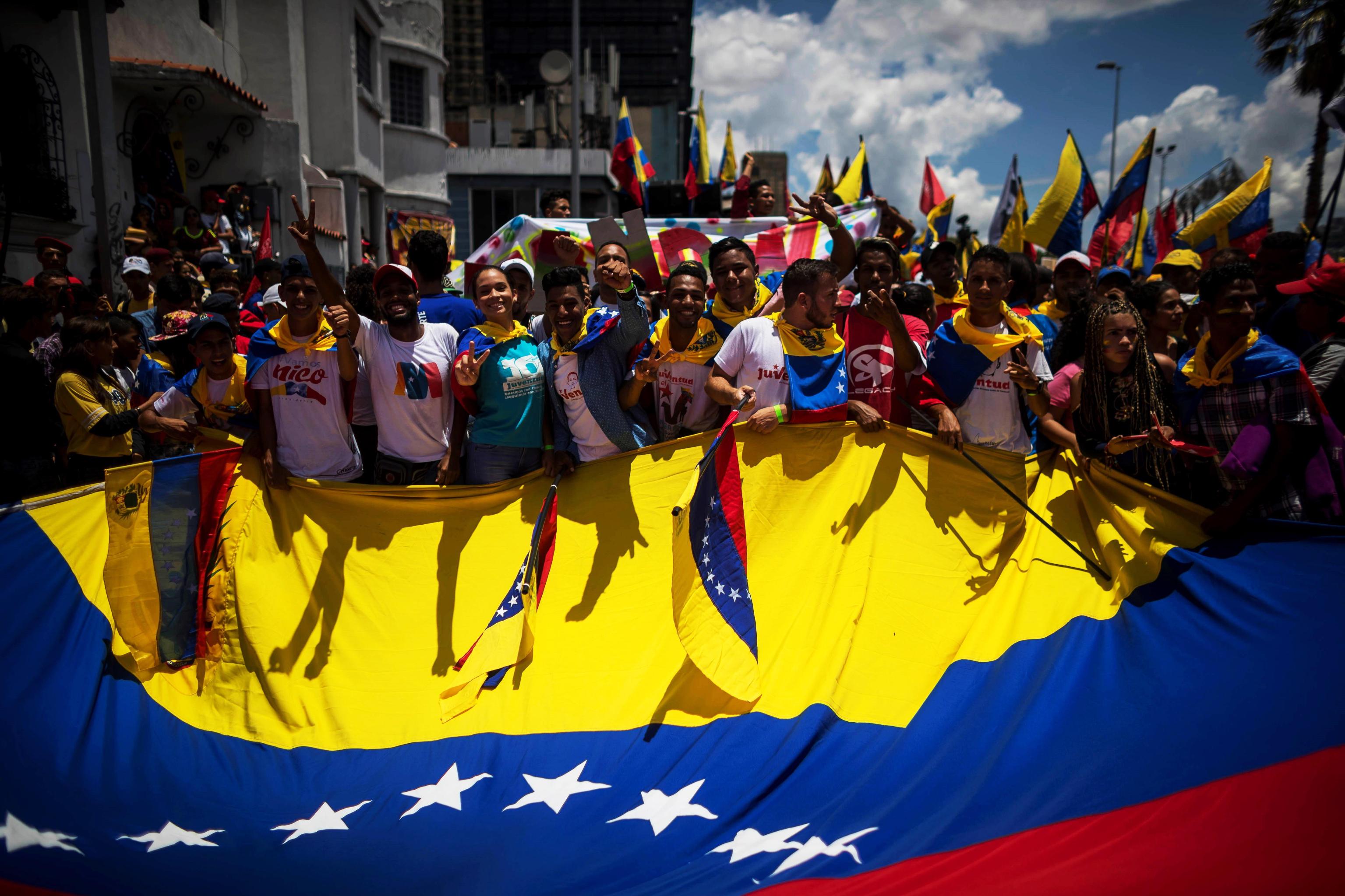 Uno scatto in cui i manifestanti si riuniscono intorno a una grande bandiera del Venezuela Uno scatto in cui i manifestanti si riuniscono intorno a una grande bandiera del Venezuela