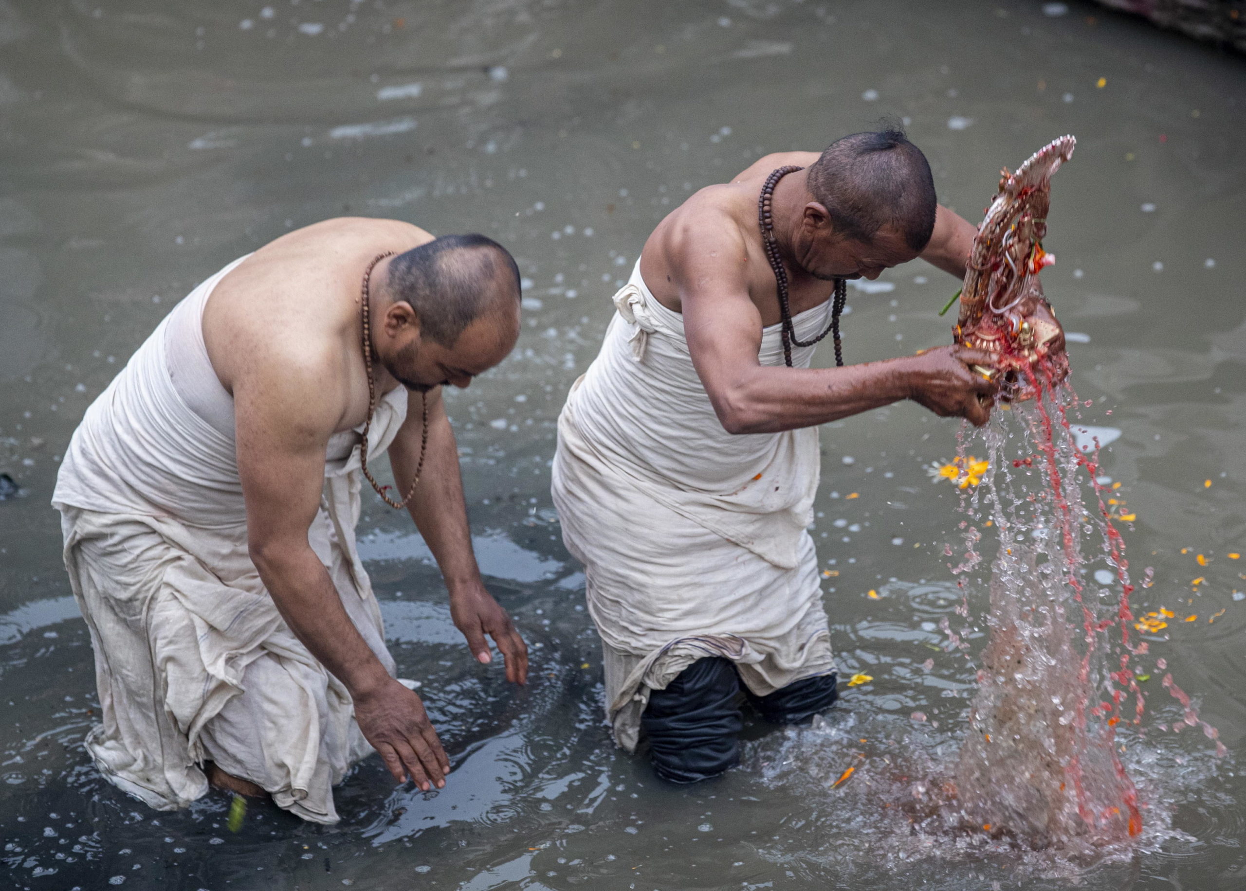 Due preti immergono un idolo nel fiume