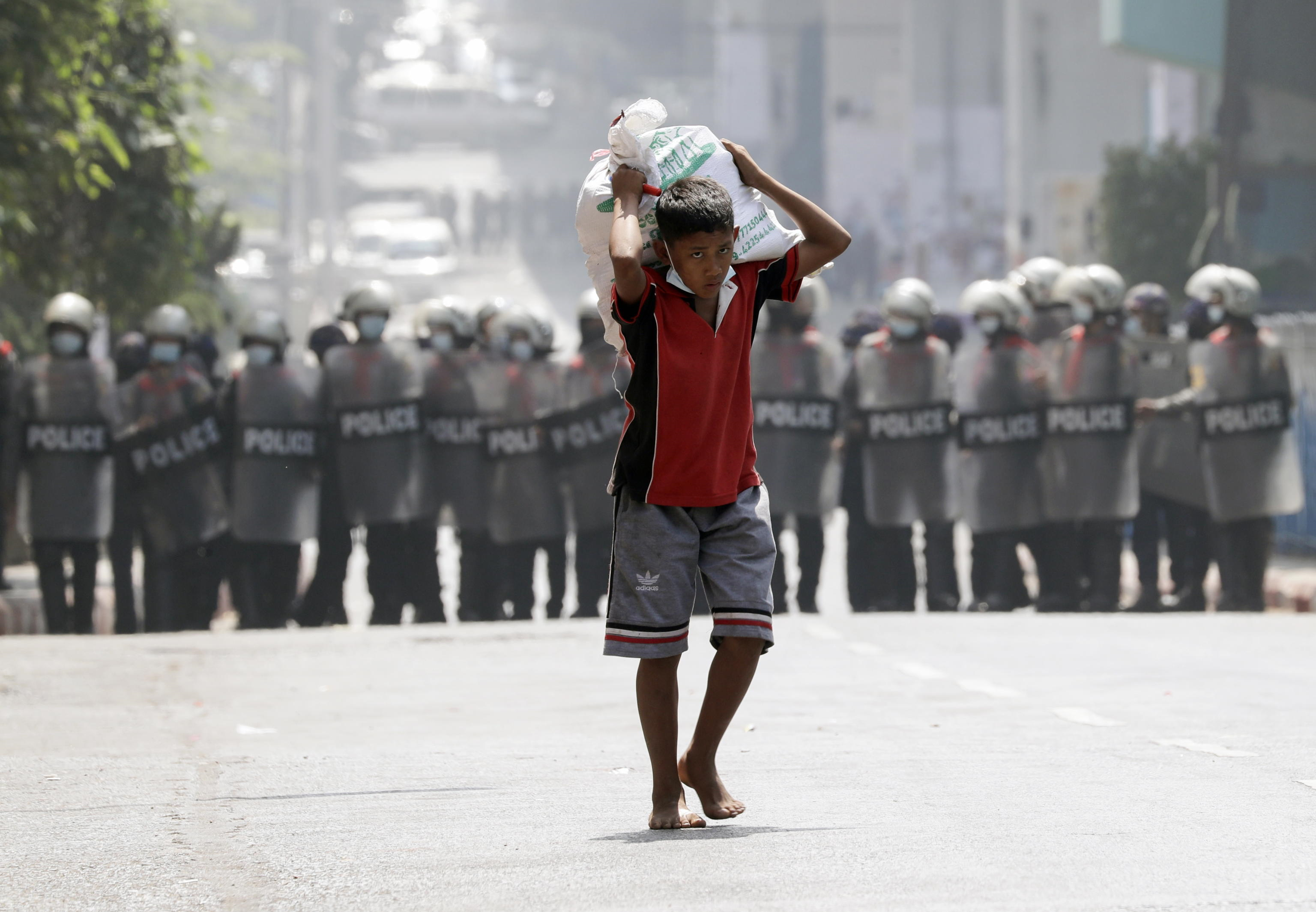 Un ragazzo trasporta un sacco di riso davanti agli agenti di polizia anti-sommossa che bloccano una strada durante una protesta contro il colpo di stato militare, a Yangon, Myanmar, 26 febbraio 2021.