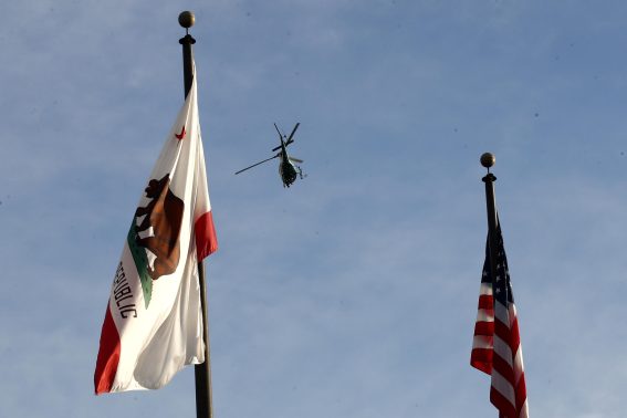 Un elicottero del dipartimento dello sceriffo vola tra una bandiera della California e una bandiera americana