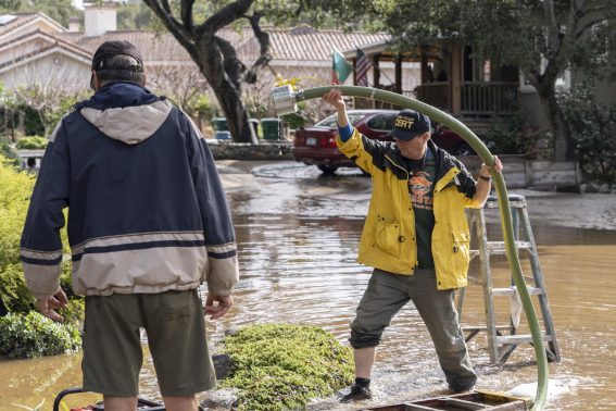 Vicini intenti a pompare via l'acqua dalla loro casa dopo un'altra ondata nella Carmel Valley